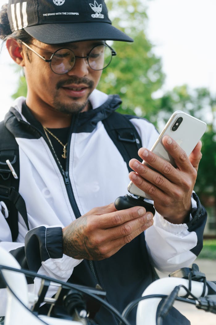 About A young man charges his smartphone using a portable charger while outdoors.